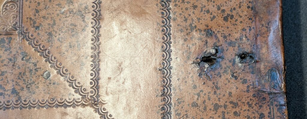 Close up of leather front cover of book with two rough holes where the chain was previously attached.