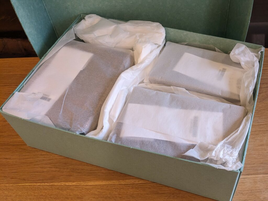 Books wrapped in tissue paper neatly packed into a green cardboard box. The box is padded with extra tissue paper.